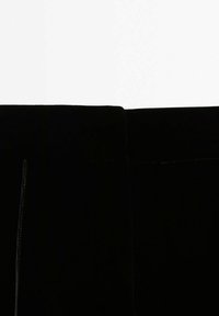 Pantalon en velours noir avec une texture lisse, taille haute et design simple avec une fermeture éclair dissimulée. Coutures minimales et aucune quincaillerie visible.