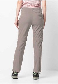 Leichte, beige Wanderhosen mit geradem Schnitt, ausgestattet mit Reißverschlusstaschen und hochrollbaren Säumen. Getragen mit schwarzen Schuhen.