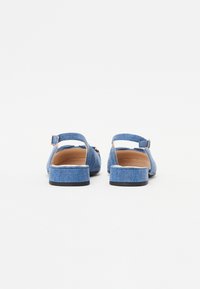 Modré denimové slingback topánky s malým blokovým podpätkom, ozdobené detailom pracky a hladkým vnútorným podšívaním. Mäkká textúra, ležérny dizajn.
