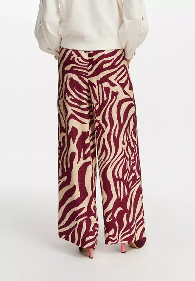 Pantalones de pierna ancha en crema con un patrón de cebra en burdeos. Textura suave con un diseño de cintura alta y bolsillos laterales. Calzado rosa visible.