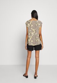 Kortärmad topp med ett blommigt och leopardmönster i beige, svart och gult, ihopparad med svarta shorts. Slät tygtextur.