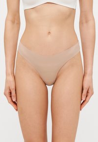 Nude stringtrosor i glatt material med låg midja, med en sömlös design och minimal täckning.