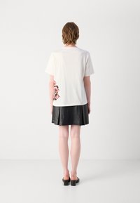 T-shirt blanc à manches courtes avec un design floral au dos, associé à une jupe en cuir plissée noire et des chaussures à talons carrés noires.