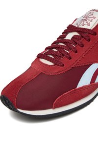 Roter Sportschuh aus einer Mischung aus Wildleder und Nylon, mit runden Schnürsenkeln und einem hellblauen Akzent auf einer dunklen Sohle.