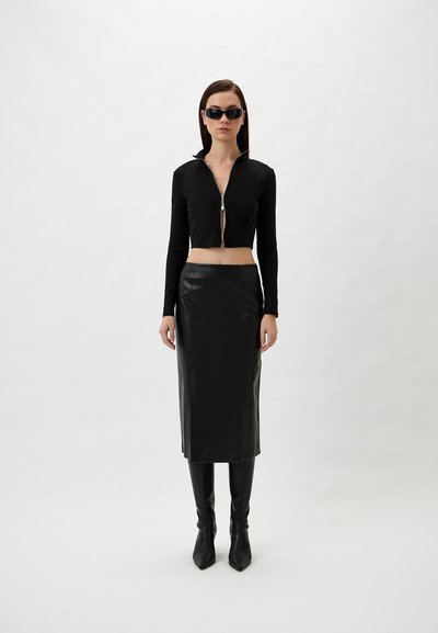 Black cropped zip-up top with long sleeves, paired with a knee-length black leather skirt and knee-high pointed boots.