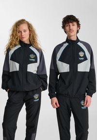 Svart och grå sportiga träningsdräkter med zippered jackor och elastiska byxor; med logotypdetaljer och färgblockerat mönster.