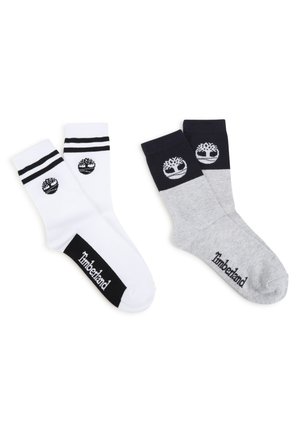 Deux paires de chaussettes en coton : blanches avec des rayures noires et un logo, grises avec des accents bleu marine et un logo. Les deux ont des bords côtelés et des détails de logo.
