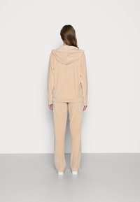 Beige veluuritakki hupparilla ja löysät housut. Ominaisuuksina pehmeä rakenne ja minimalistikko muotoilu ilman kuvioita.