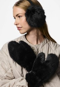 Orejeras y mitones de piel sintética negra, con una textura suave, formas redondeadas y longitudes variadas, combinados con una chaqueta acolchada de color beige claro.