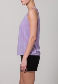 Lilac sleeveless top with embroidered detailing on front, made of lightweight fabric, paired with black shorts, side view.