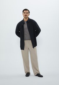 Black button-up shirt over a gray ribbed sweater, paired with beige wide-leg trousers and black shoes. Simple design, smooth textures.