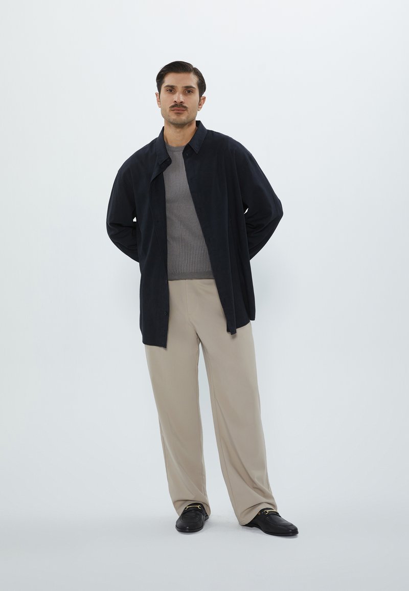 Black button-up shirt over a gray ribbed sweater, paired with beige wide-leg trousers and black shoes. Simple design, smooth textures.