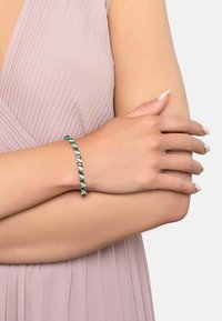 Silver bracelet featuring green gemstones in an alternating leaf shape design, worn on a wrist with a soft beige skin tone.