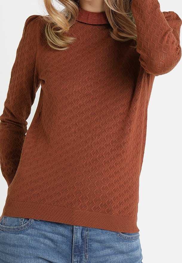 Pull à manches longues de couleur rouille avec un motif losange texturé, col rond et ourlet côtelé. Associé à un jean bleu.