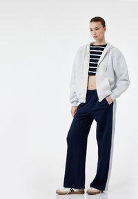 Grå zip-hoodie over en marineblå stribet crop top, parret med marineblå brede bukser med grå sidelæg og hvide sneakers.