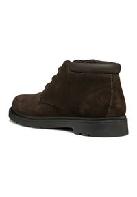 Stivali ankle in suede marrone con un morbido bordo in pelle di un marrone scuro, punta rotonda e suola in gomma nera. Caratterizzati da lacci e dettagli di cucitura minimi.