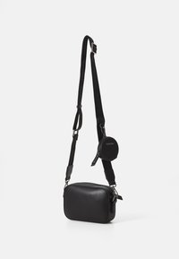 Sac en cuir noir en bandoulière, de forme rectangulaire, avec une bandoulière réglable et une petite pochette ronde attachée ; texture lisse avec fermeture éclair.