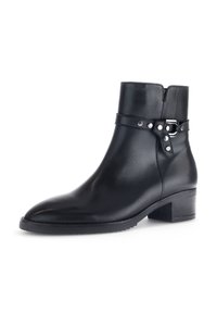 Bottines en cuir noir avec un bout arrondi, un petit talon carré et une sangle décorative avec des accents métalliques. Texture lisse.