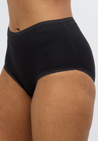 Μαύρο βαμβακερό εσώρουχο με ψηλή μέση, διακοσμημένο με δαντέλα σε κυματιστό τελείωμα κατά μήκος της μέσης και των ανοίξεων στα πόδια, με λεία υφή.