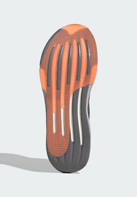 Suola di una sneakers con una base in gomma nera testurizzata accompagnata da accenti arancioni e grigi, comprendente distinti motivi di battistrada e scanalature bianche.