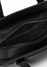 Interno di una borsa in pelle nera con una texture, dotato di un compartimento con zip. Presenta un rivestimento liscio e molteplici tasche per l'organizzazione.