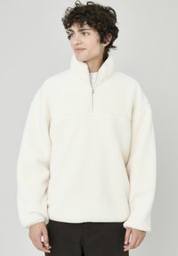 Pull en polaire couleur crème avec un col haut et une fermeture éclair demi-zippée. Caractéristiques : coupe décontractée et tissu doux et texturé.