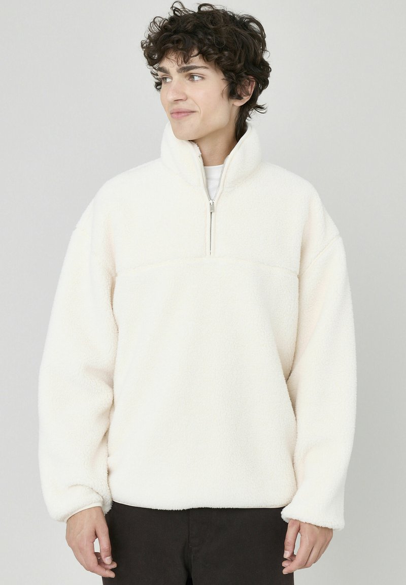 Pull en polaire couleur crème avec un col haut et une fermeture éclair demi-zippée. Caractéristiques : coupe décontractée et tissu doux et texturé.