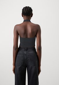Črn halter crop top iz gladke tkanine, v kombinaciji z visokot sentim črnimi kavbojkami s žepi in blagim zbledelostjo na stegnih.
