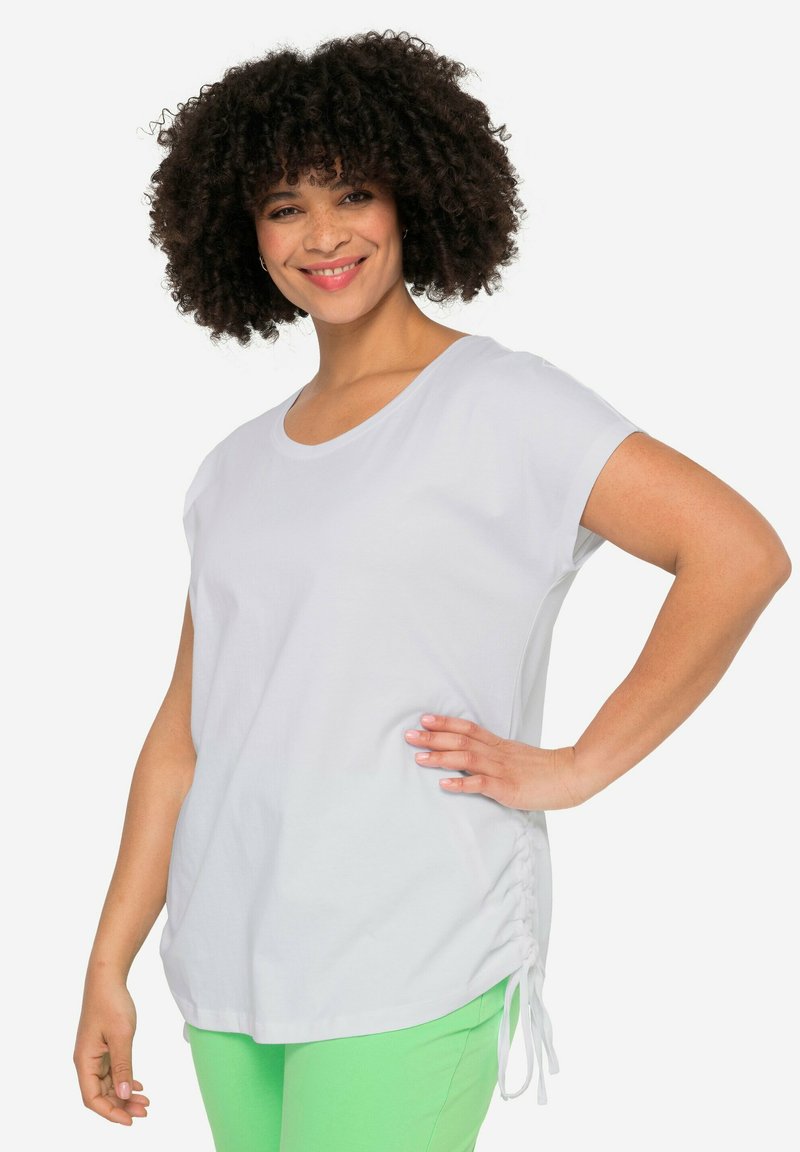 Camiseta blanca de manga corta con escote redondeado y lazos laterales. Fabricada con una tela suave, presenta un corte relajado y una textura lisa.