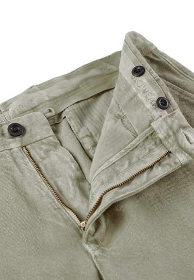 Khaki corduroy broek heeft een ritssluiting en twee knopen, met een visgraatstructuur en een discreet merkembleem dat aan de binnenkant is gestikt.