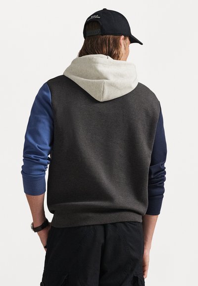 Sweatshirt with capuz apresentando um corpo cinza, mangas azuis e um capuz cinza. Feito de um tecido macio com punhos canelados. Um boné preto é usado.