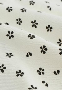 Vitt tyg med en mjuk textur som har ett upprepat mönster av små svarta blommor och petalformer, vilket skapar en delikat design.