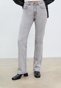 Sive traperice ravnog kroja, visokog struka, s pet džepova i suptilnom teksturom, uparene s crnim čizmama s potpeticom.