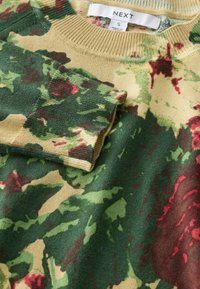 Groen en beige camouflage sweater met rode accenten, geribbelde kraag en zachte textuur. Label toont "NEXT" en maat "S." Gedetailleerde print overal.