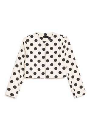 Veste blanche courte à manches longues avec un motif de pois noirs, encolure ronde, sans boutons ni fermetures visibles.