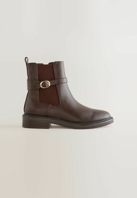Bottine en cuir marron foncé avec talon bas superposé, panneaux latéraux élastiques et une bride décorative avec boucle dorée.