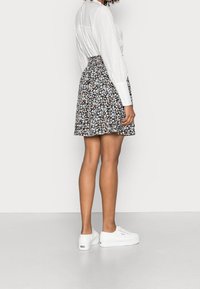 Blumenmusterrock mit schwarzem Hintergrund, plissierter Design und hohem Taillenbund. Kombiniert mit weißen Sport Sneakers.