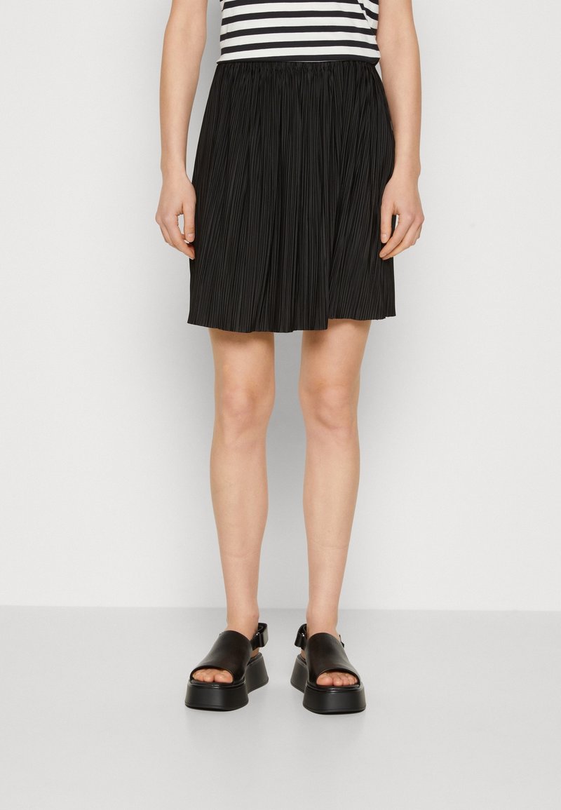 Schwarzer plissierter Rock mit elastischem Bund, kombiniert mit schwarzen Plateausandalen. Die Sandalen haben einen breiten Riemen und ein offenes Zehendesign.