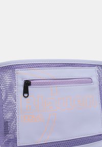 Borsa a rete viola con dettagli in pelle bianca. Presenta una tasca frontale con zip e il logo "Blauer USA" in arancione. Texture liscia e design moderno.