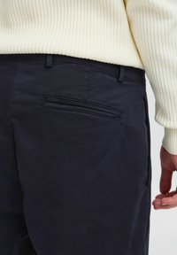 Navy fabric trousers featuring a flat back pocket and a subtle textured finish, paired with a light ribbed sweater.