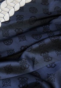 Tessuto blu navy con una superficie liscia e un design decorato da motivi scuri, compresi forme geometriche ed emblemi, disposti in modo uniforme.