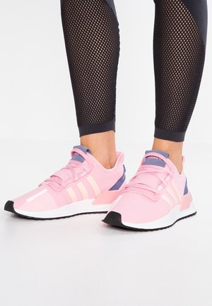 Fødder iført pink og lilla Adidas-sneakers med hvide såler og sorte ydersåler, kombineret med sorte mesh-leggings.