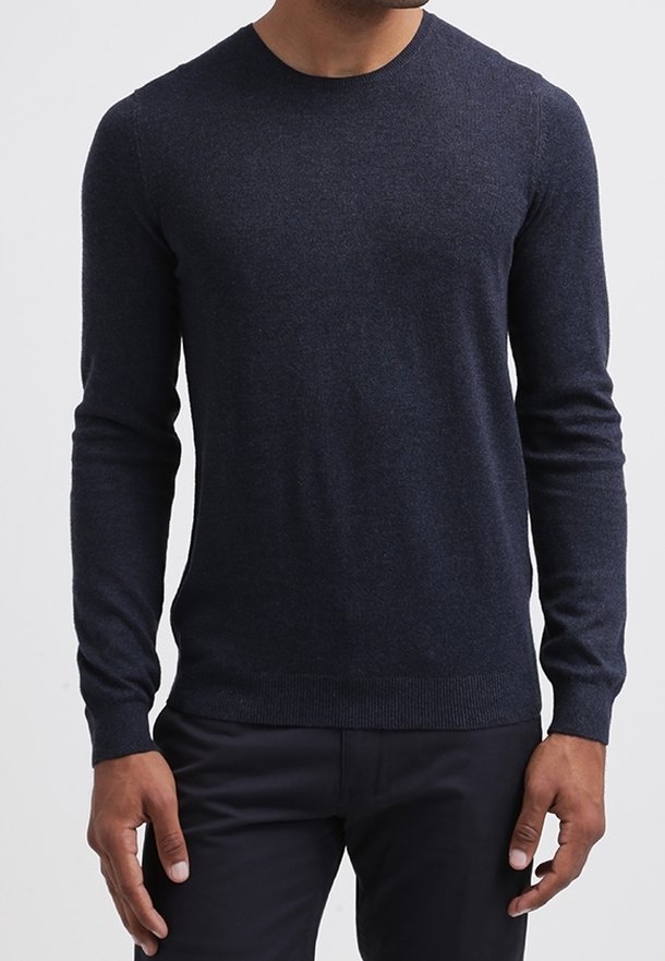 Homme portant un pull moulant à manches longues de couleur bleu marine foncé avec un col rond et un pantalon noir, debout les bras détendus le long du corps.