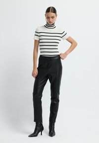 Zwart-wit gestreepte rib gebreide coltrui, gecombineerd met op maat gemaakte zwarte leren broeken en spitse enkelboots. Strak, minimalistisch ontwerp.