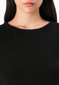 Crni rebrasti pleteni top s okruglim izrezom, koji ima teksturirani uzorak koji stvara vertikalne linije na tkanini.