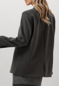 Tummanharmaa bleiseri, jossa on sileä pinta, jämäkkä muoto ja takana oleva yksittäinen halkio; siinä on hoikat hihat ja napitetut hihansuut.