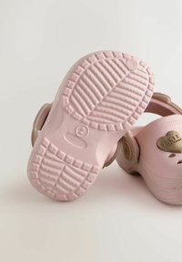 Roosa kummist sussid tekstureeritud talladega ja reguleeritavate külgrihmadega. Omavad kuldset südamekujulikku logo ja tuulutusavasid külgedel.