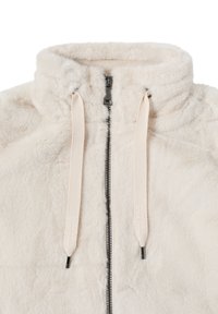 Veste zippée en fausse fourrure beige clair, avec un col haut, une fermeture éclair noire et des cordons de serrage crème avec texte embossé. Texture douce et pelucheuse.