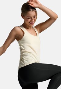 Top in beige chiaro con scollo rotondo e spalline larghe, abbinato a leggings neri. Il materiale sembra liscio con cuciture minime.