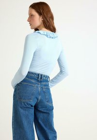 Ljusblå långärmad topp med ruffles vid halsringningen, ihop med högmidjade blå denimjeans med bakfickor.